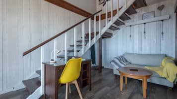 Eine Treppe mit hölzernen Geländern, ein Essbereich mit einem gelben Stuhl, einem runden Holztisch und einem grauen Sofa mit gelber Decke.