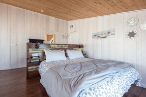 Un dormitorio con cabecera de madera, cama con ropa de cama estampada, mesita de noche y lámpara de pared.
