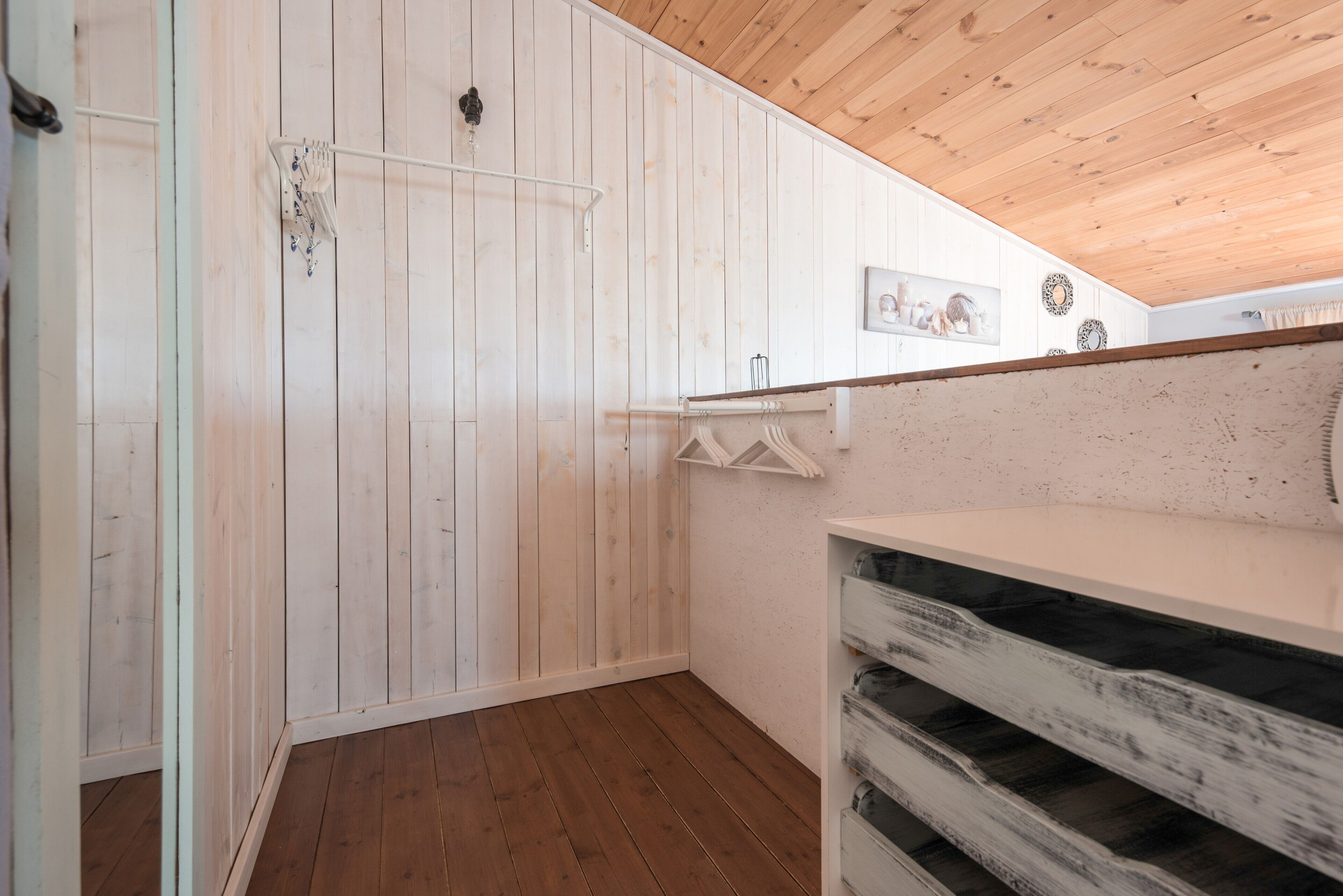A room with wooden walls, a wooden ceiling, and a white shelf with storage bins.