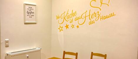 Ein Essbereich mit Holztisch und -stühlen, einem Heizkörper und einer Wand mit einem dekorativen Schild.