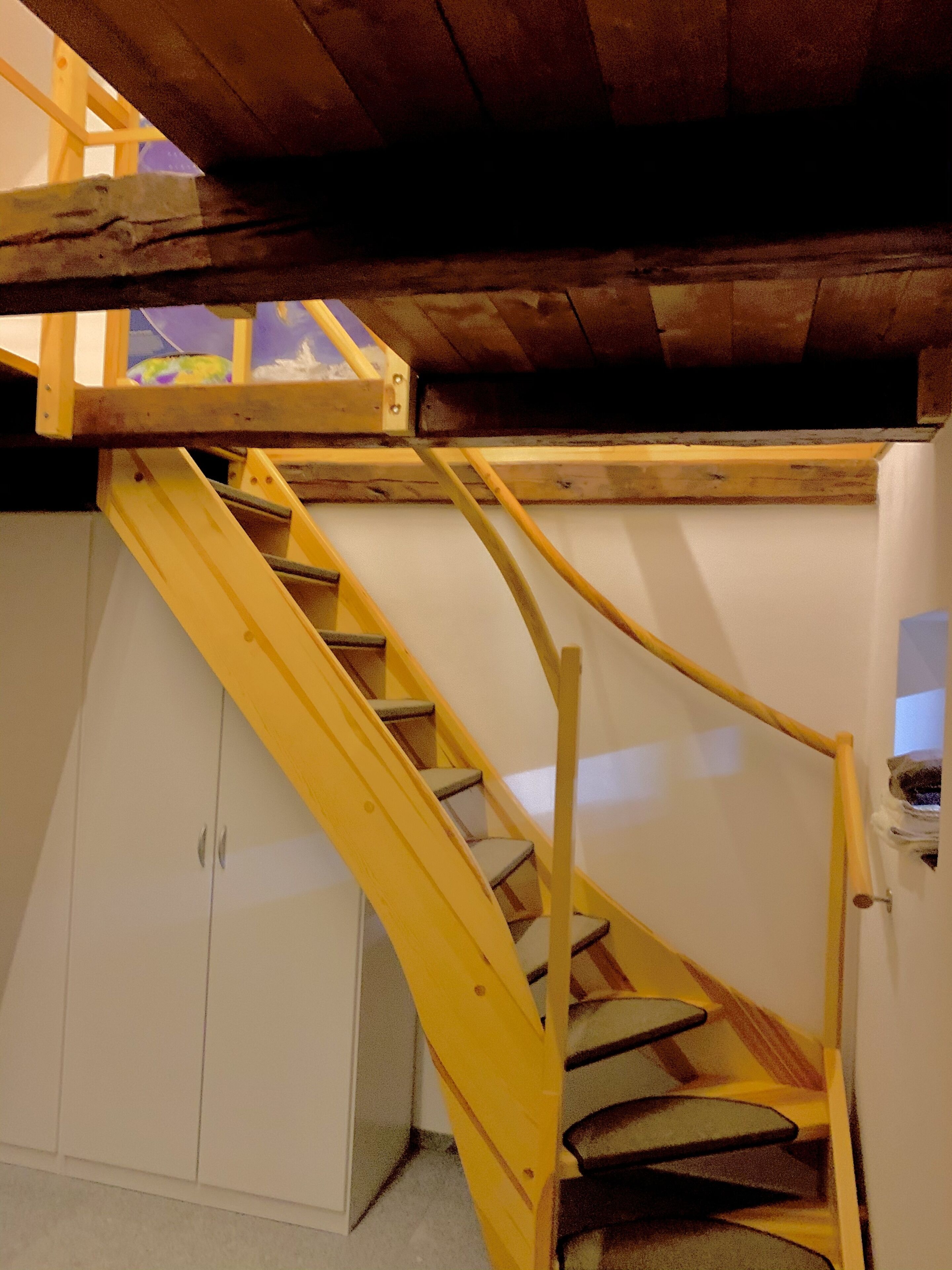 A wooden staircase with a yellow handrail leading to a lofted area.