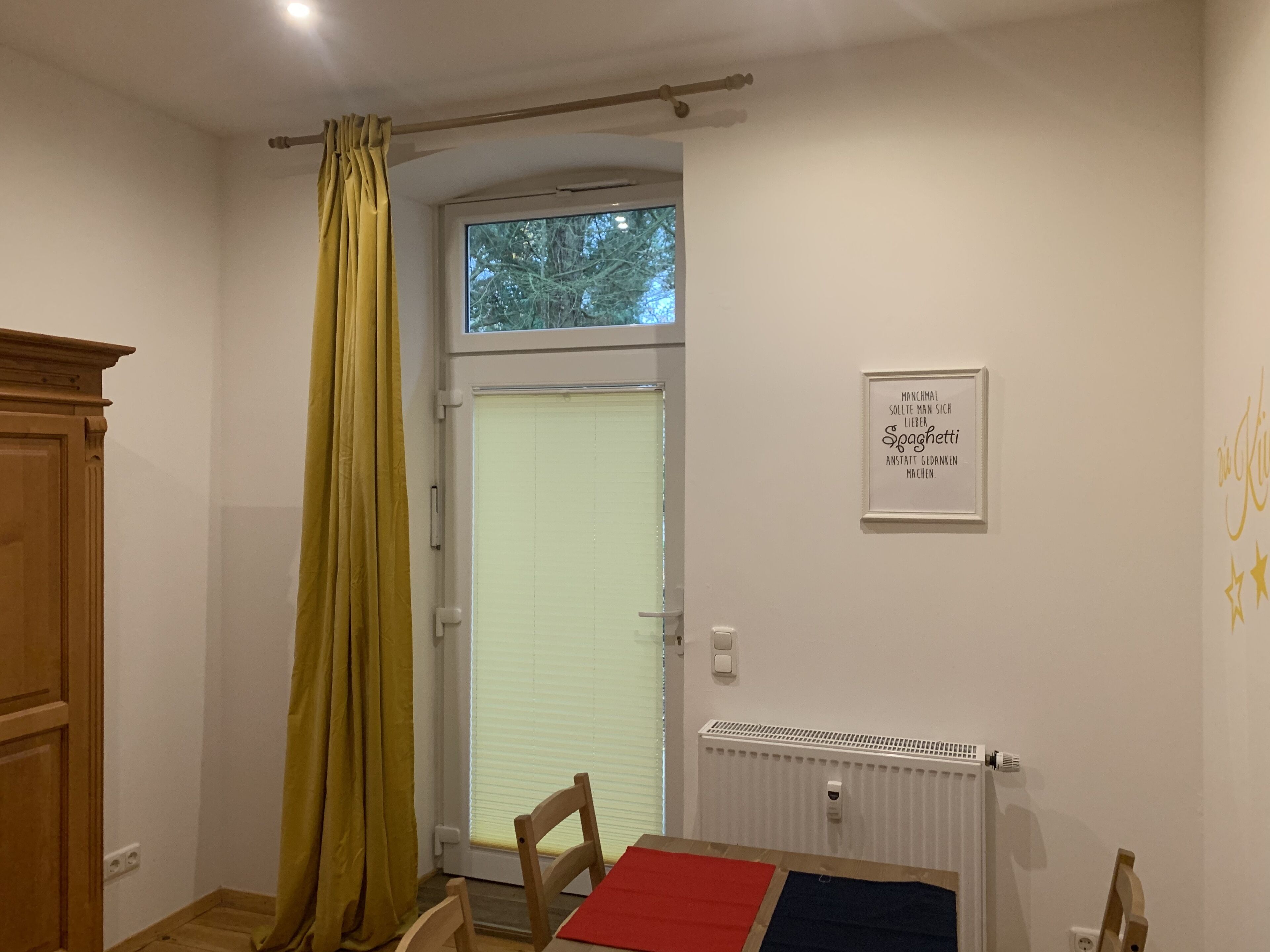 A room with a window, a radiator, a framed quote on the wall, and a wooden door.