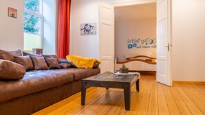 A cozy living room with a brown leather sofa, a wooden coffee table, and a large window with red curtains. - Seasides Villa Kunterbunt (Scharbeutz)