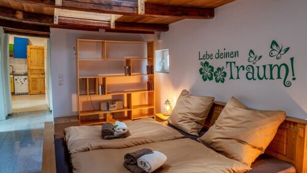 A cozy bedroom with a wooden ceiling, a bed with beige bedding, and a wall with a motivational quote. - Seasides Villa Kunterbunt (Scharbeutz)