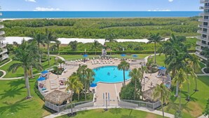 Een resort met een centraal gelegen zwembad, omringd door palmbomen en ligbedden, met uitzicht op een strand en de oceaan.