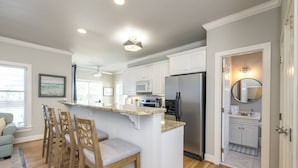 A modern kitchen with white cabinets, a stainless steel refrigerator, and a bar area with bar stools.