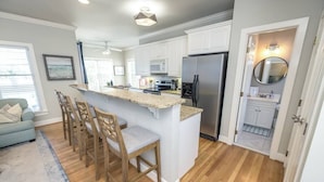 A modern kitchen with white cabinets, a granite island with bar stools, a stainless steel refrigerator, and a microwave.