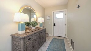 A hallway with a wooden console table, two wall-mounted lamps, a mirror, a door, and a blue rug.