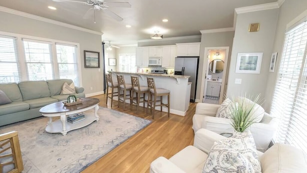 A spacious living room with a sofa, coffee table, and chairs, a kitchen with a bar area, and a ceiling fan.