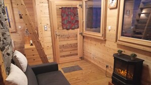 Interior acogedor de una cabaña con piso de madera, un sofá con cojines, una chimenea y una ventana con cortinas.
