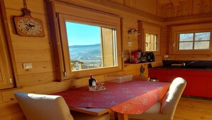 Una cabaña de madera con una mesa de comedor, sillas, zona de cocina y un ventanal con vistas al campo.