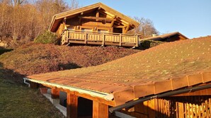 Una cabaña de madera con balcón, ubicada en una ladera con techo inclinado.