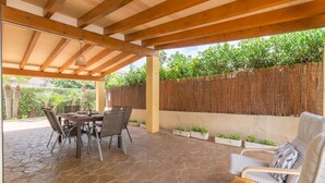 A covered patio with a stone floor, wooden ceiling beams, a table with chairs, and a seating area with cushions. - Holiday house with private pool only 200m to the beach, Cala Ratjada, Mallorca (Cala Ratjada)
