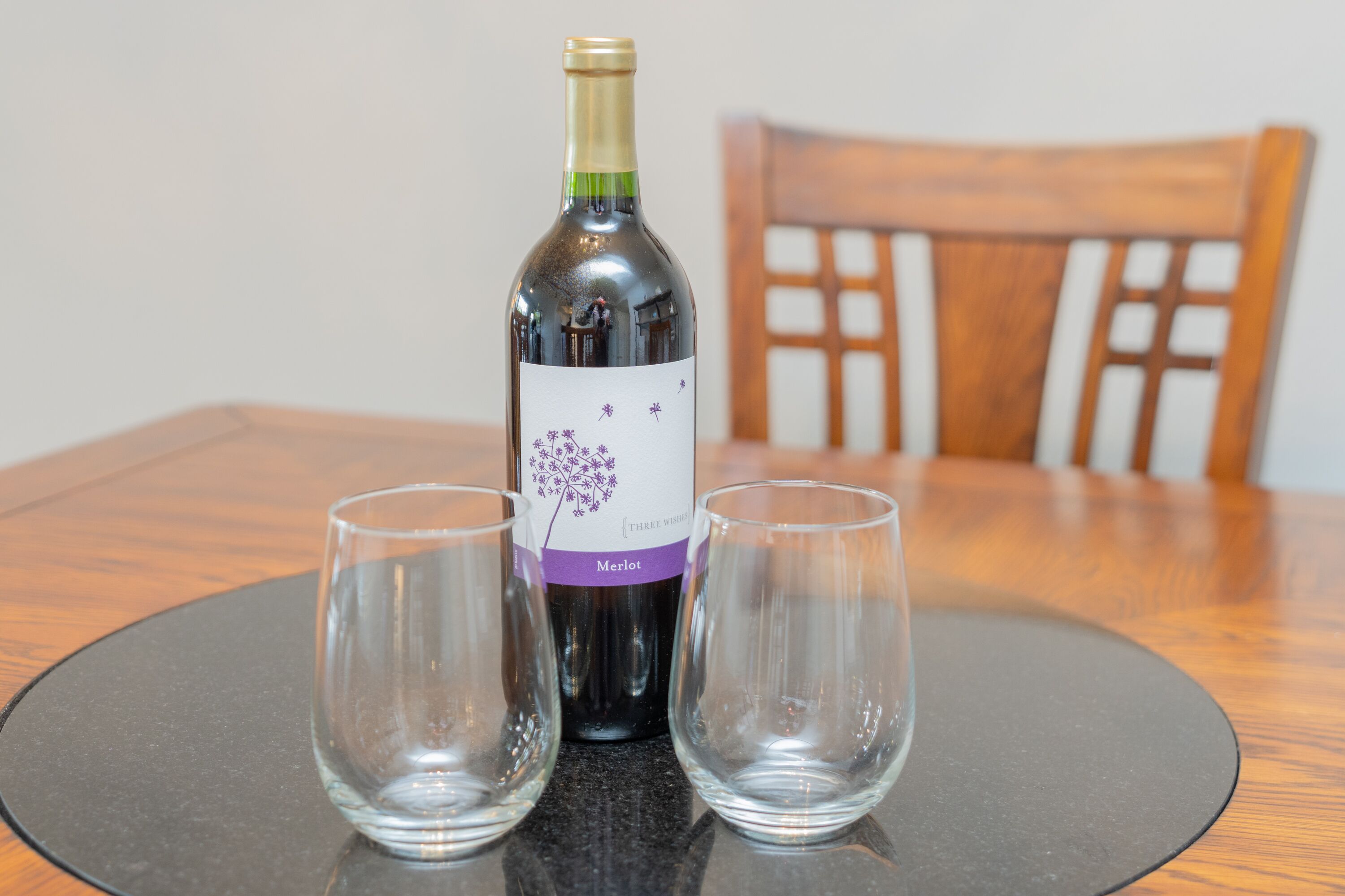 A bottle of Merlot wine on a round table with two empty glasses.
