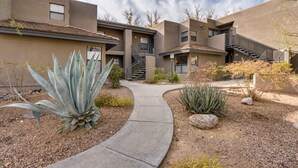 Un edificio residencial con un sendero curvo, escaleras y un jardín ajardinado con plantas de agave.