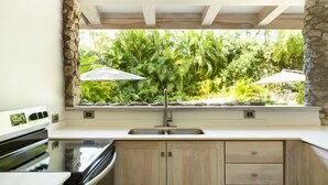 A kitchen with a stone accent wall, a built-in stove, and a window overlooking lush greenery. - Luxurious Ganesh Villa (Nicoya)