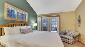 Quarto com cama grande, sofá xadrez, janela com vista e porta para o exterior.