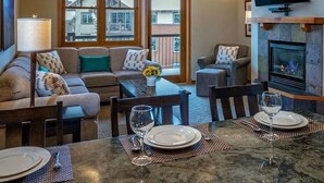 A cozy living room with a fireplace, a dining area with a table set for two, and a large window with a view of the outside. - Ski-In/Ski-Out Luxury at Grand Timber Lodge – Breckenridge, CO (Breckenridge)