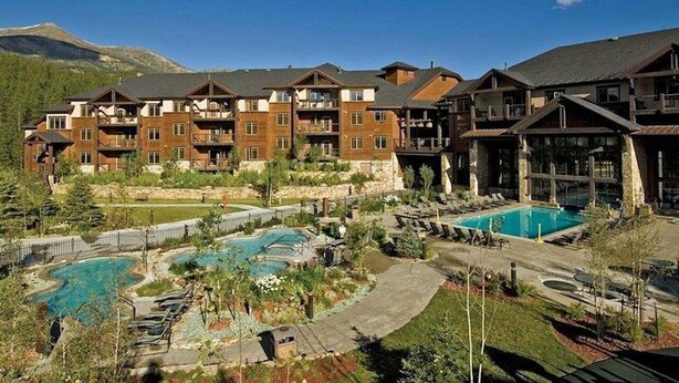 A hotel with multiple floors, a pool area, and a mountainous backdrop. - Ski-In/Ski-Out Luxury at Grand Timber Lodge – Breckenridge, CO (Breckenridge)
