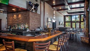 A bar area with a stone wall, multiple liquor bottles, a TV screen, and several wooden chairs. - Ski-In/Ski-Out Luxury at Grand Timber Lodge – Breckenridge, CO (Breckenridge)