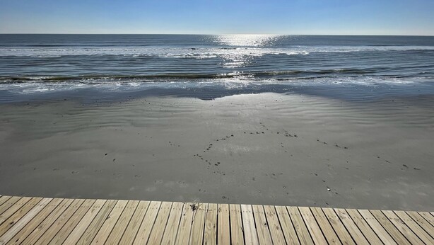 Una terrassa de fusta que condueix a una platja amb ones tranquil·les i un cel serè.