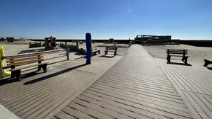 Una passera de fusta que condueix a una platja, amb bancs i una construcció blava.