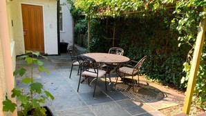 Un pati amb una taula rodona i cadires, envoltat d'un paviment de pedra i una porta de fusta.