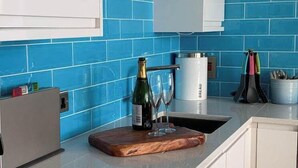 Een keuken met blauwe tegels, een houten snijplank, een fles champagne en een koffiezetapparaat.