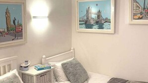 Een slaapkamer met een bed, een nachtkastje met een boek, en twee foto’s in lijsten aan de muur.