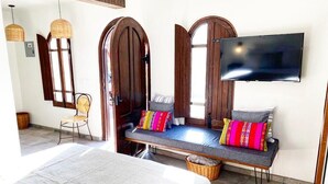 A room with a bed, a bench with colorful cushions, a television, and a wicker basket. - Loreto80-NEW Studio Palma, in downtown by beach (Loreto)