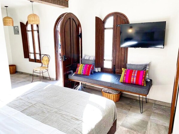A room with a bed, a bench with colorful cushions, a television, and a wicker basket.