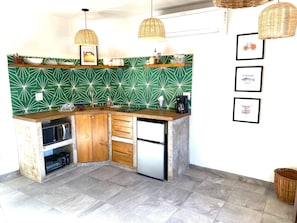 Compact kitchen with microwave, stainless steel refrigerator, and sink with faucet, illuminated by pendant lights.