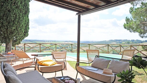 Un área de estar al aire libre con sillones de descanso y una mesa, con vistas a un paisaje pintoresco que incluye una piscina.