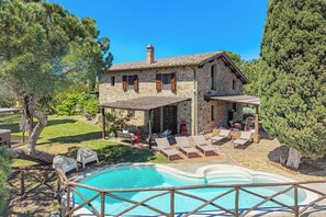 A stone house with a pool, outdoor seating, and a garden.