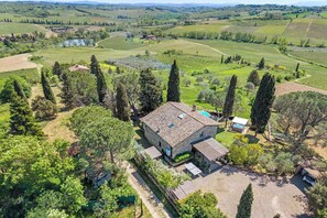 An aerial view of a stone house with a pool, surrounded by vineyards and rolling hills.