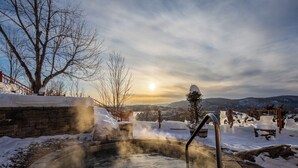 A hot spring surrounded by snow, with a view of mountains and a clear sky.