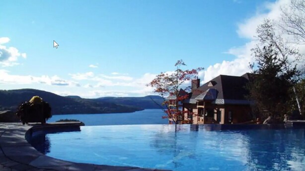 A swimming pool with a house in the background, a clear sky, and mountains in the distance.