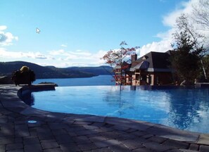 Una piscina con una casa al fondo, cielo despejado y montañas a lo lejos.