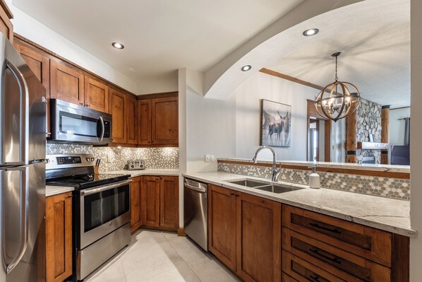 Una cocina moderna con armarios de madera, electrodomésticos de acero inoxidable, salpicadero de piedra y una isla grande con un lavamanos.