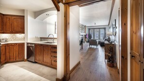 A spacious kitchen with wooden cabinets and a dishwasher, leading to a dining area with a chandelier and a bear statue.