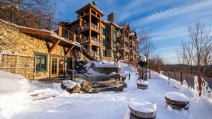 A large, multi-story lodge with stone and wood exterior, a stone staircase, and a snow-covered landscape.