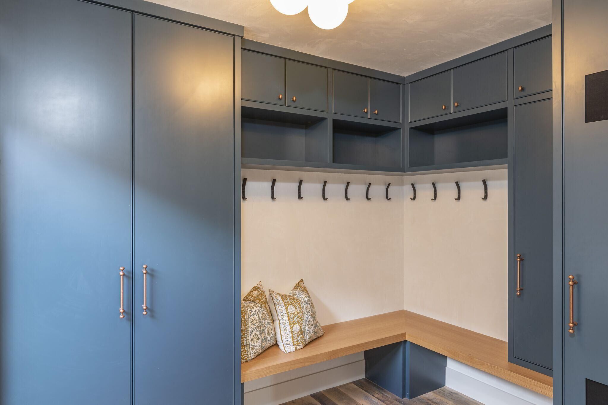 Un espace de rangement moderne avec des armoires grises, un banc agrémenté de coussins à motifs et un porte-manteau.