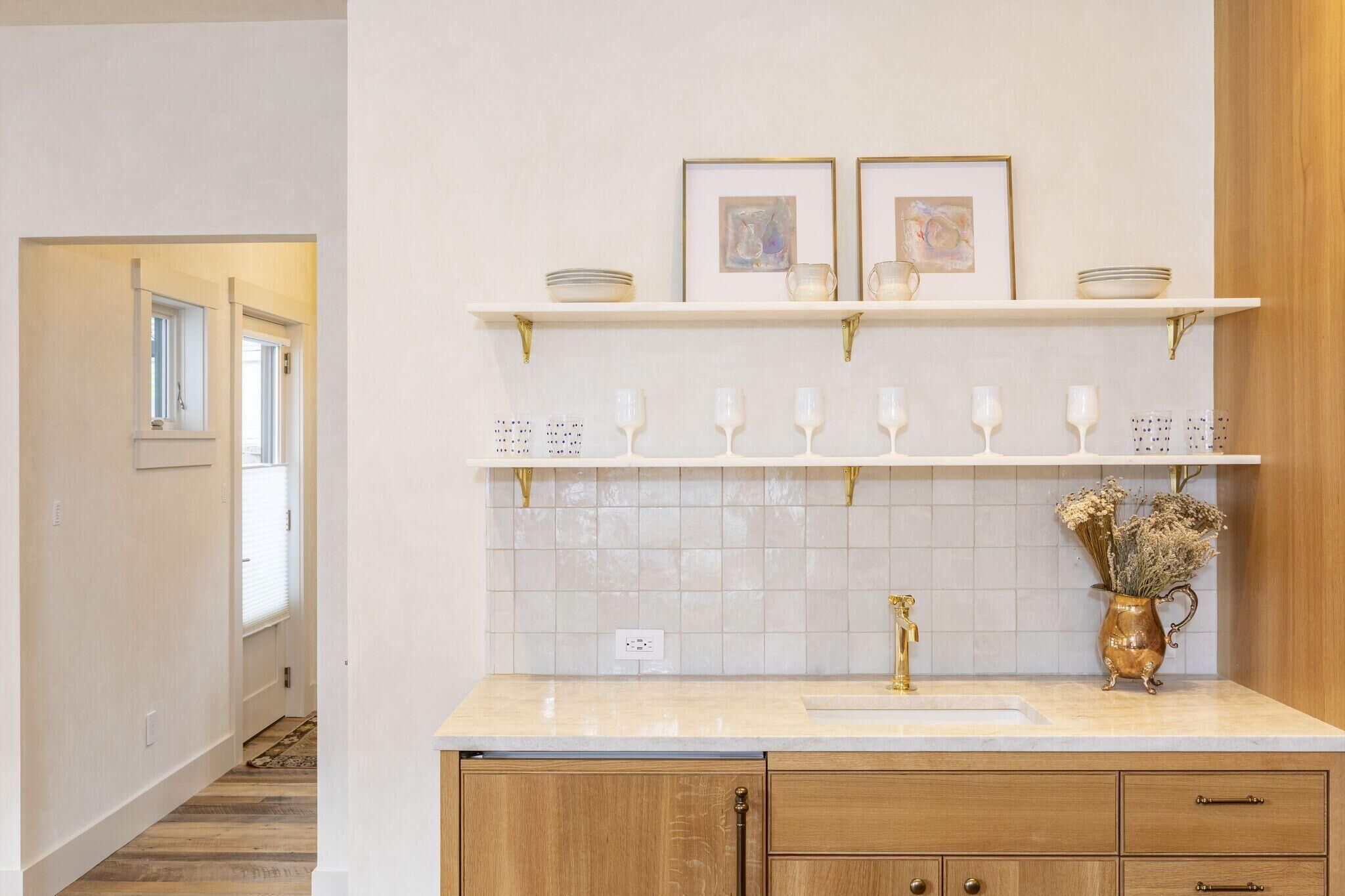 A kitchen with a white countertop, a gold faucet, and a shelf with framed pictures and decorative items.
