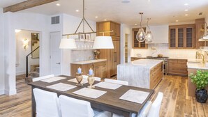 A modern kitchen with wooden cabinets, a marble island, pendant lighting, and a dining area with a wooden table and white chairs. - Splendid Home in the Heart of Telluride Town (Telluride)