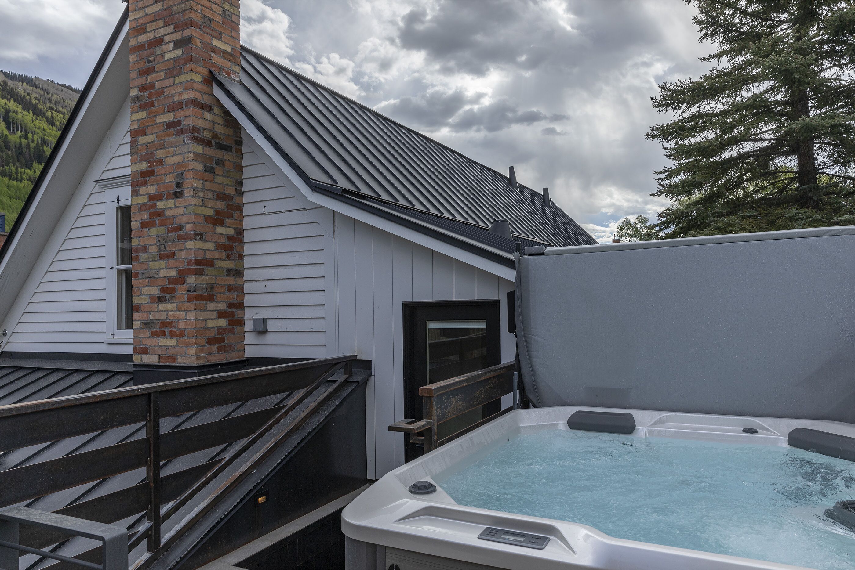 A hot tub adjacent to a building with a brick chimney and a metal roof.