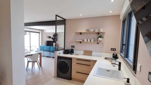 Une cuisine moderne dotée d’un lave-linge intégré, d’une grande fenêtre et d’un coin repas avec une chaise bleue.