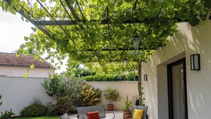 Une terrasse en bois, dotée de mobilier d’extérieur et d’une pergola recouverte de feuillage verdoyant.