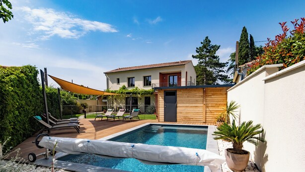 Une piscine avec des chaises longues, une terrasse en bois et un mur blanc.