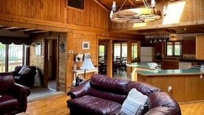 A spacious wooden cabin interior with a leather sofa, dining area, kitchen, and a large skylight.