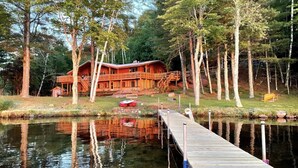 A wooden cabin with a dock extending into a calm lake, surrounded by trees.